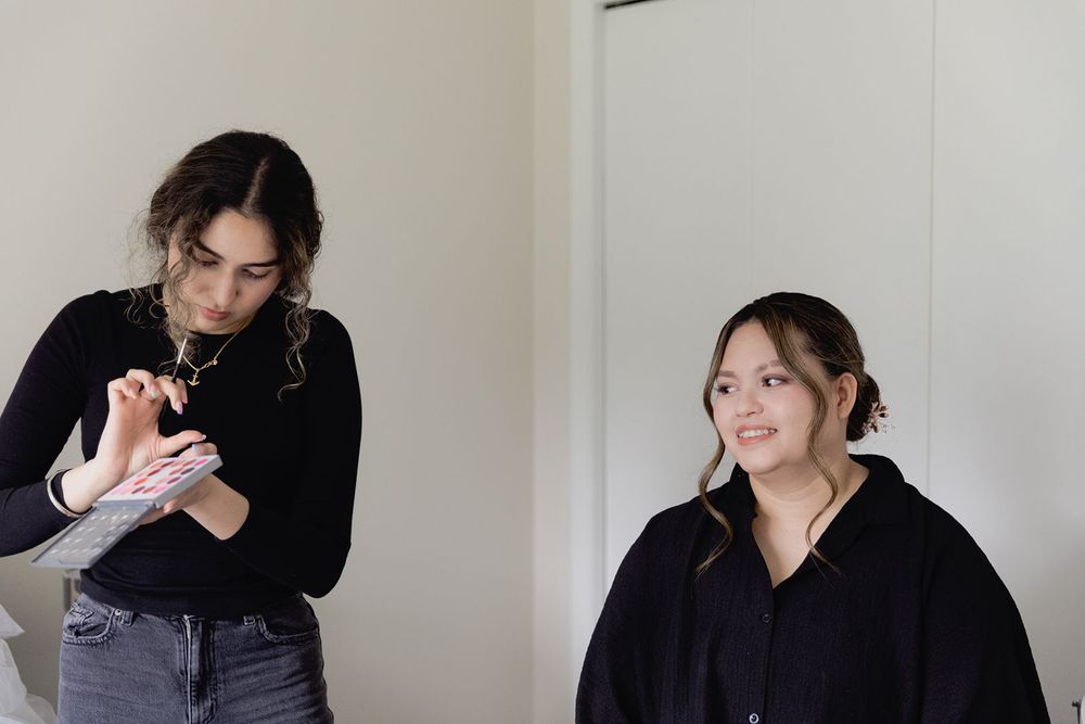 Makeup artist reviews notes while a smiling bride-to-be sits relaxed during pre-wedding preparations.