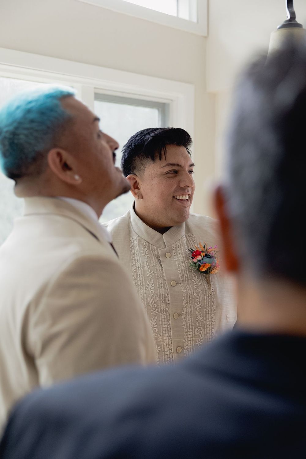 A smiling groom in an embroidered barong tagalog with a colorful boutonniere stands with wedding party members.