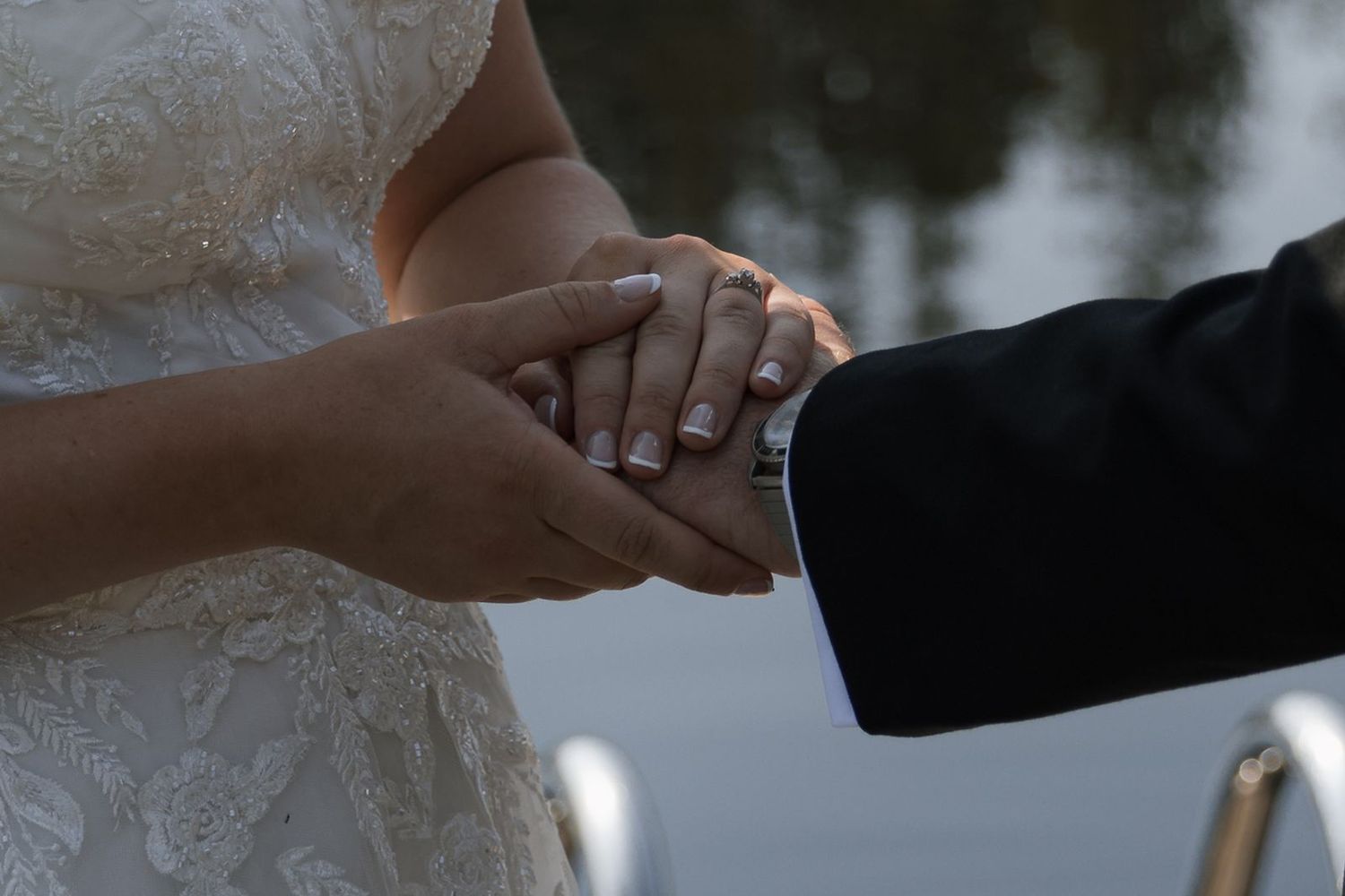 Close-up of bride and groom holding hands during wedding ceremony, showcasing wedding rings.