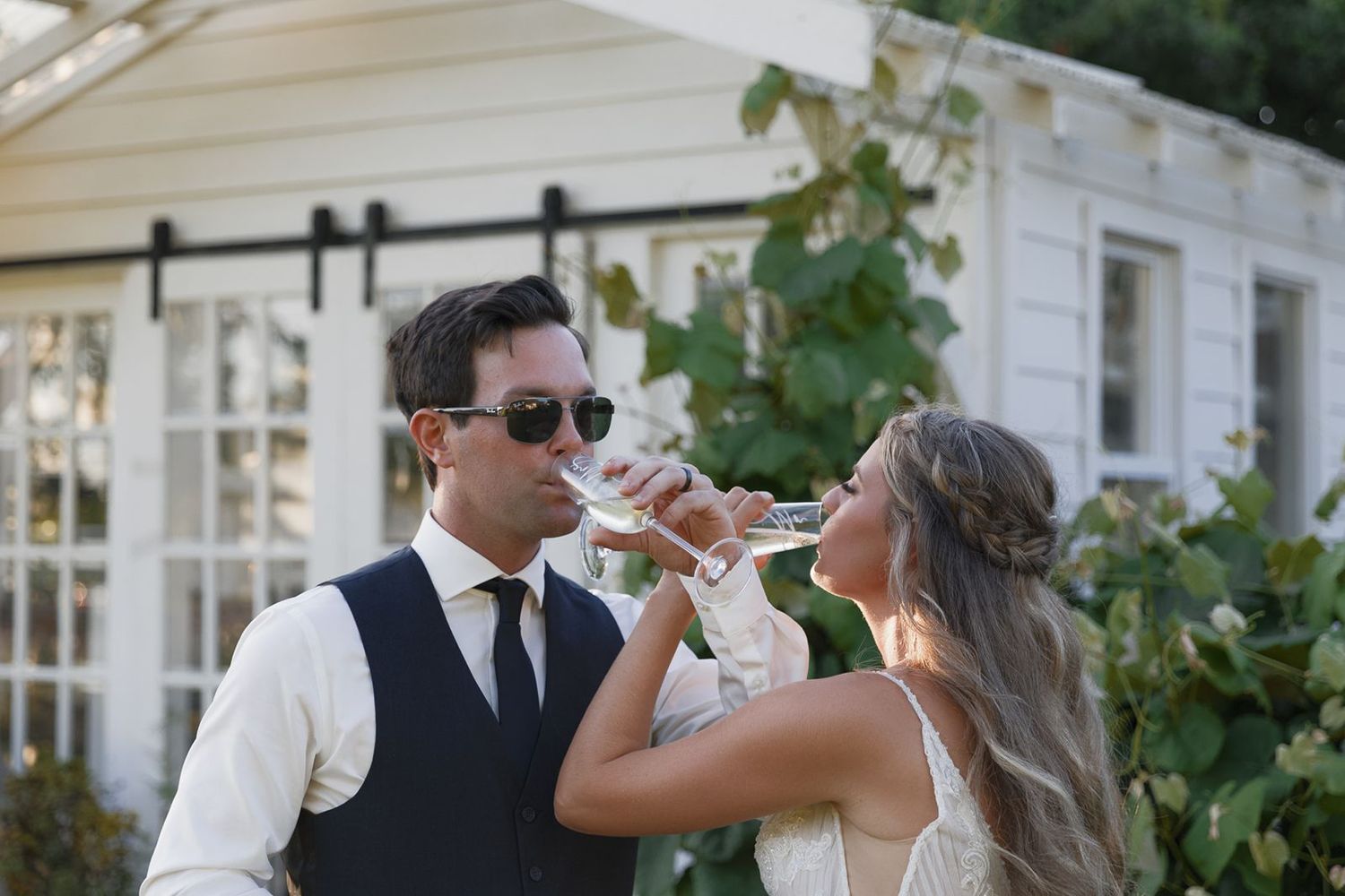Bride and groom toast with champagne glasses outside a white country house venue.