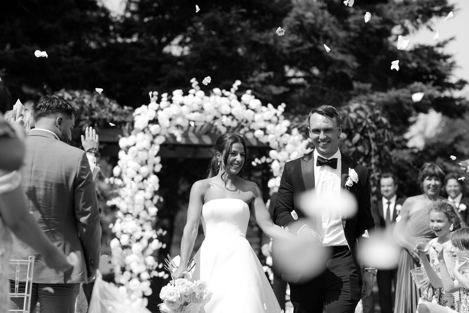 A black and white wedding celebration photo montage shows joyful moments and dancing at an outdoor reception.