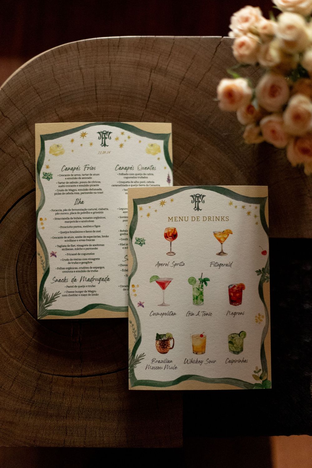Decorative wedding menu cards featuring cocktail illustrations and floral designs displayed on a dark wooden surface.
