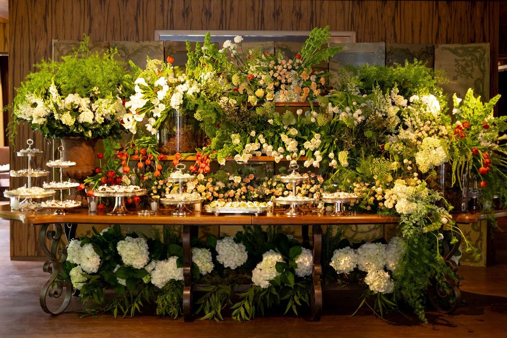 Elegant floral wedding reception table decor with white flowers and greenery spanning across a rustic wooden surface.