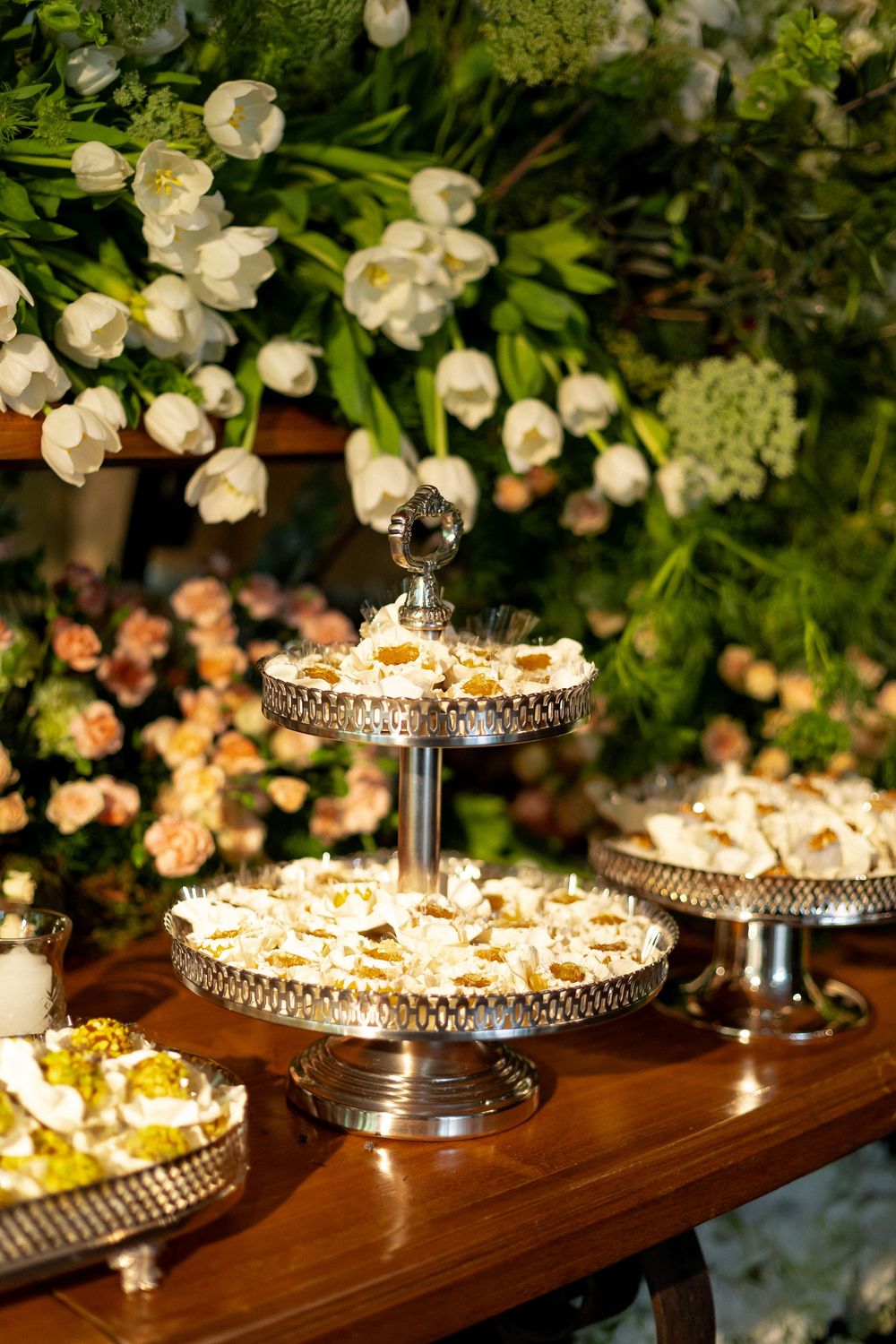 Elegant dessert display featuring tiered crystal stands with pastries and white floral arrangements above.