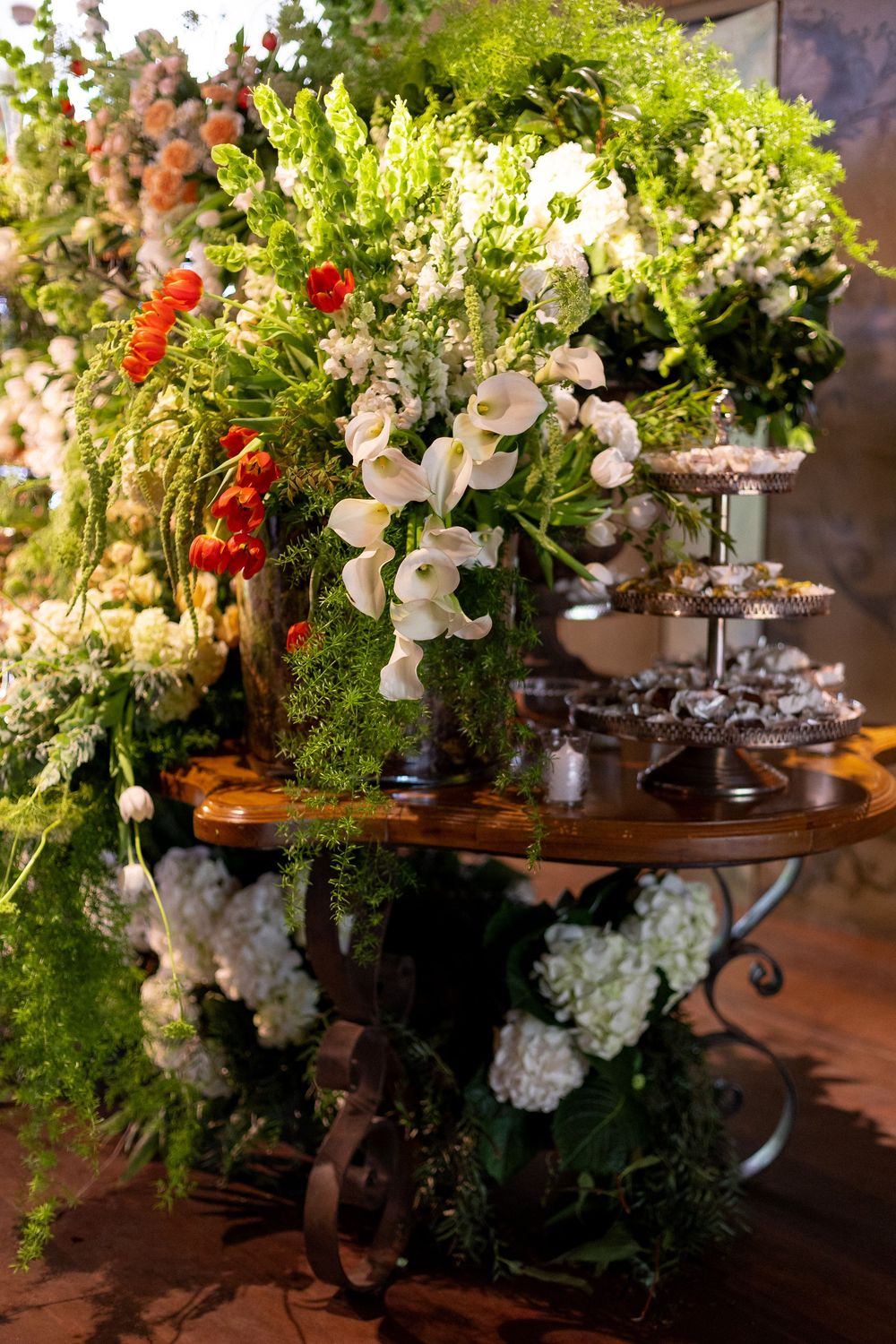 Elegant floral arrangement with white orchids and red accents displayed on an ornate wooden table with cascading greenery.