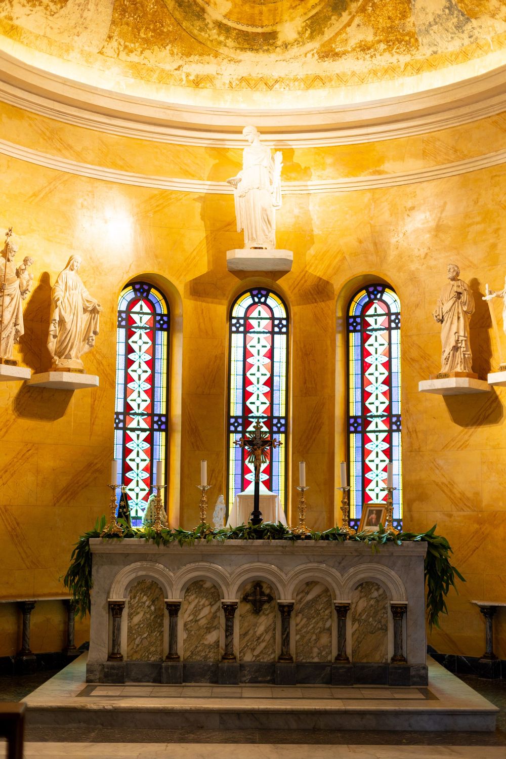 Ornate church altar with stained glass windows and golden walls illuminated in warm light.