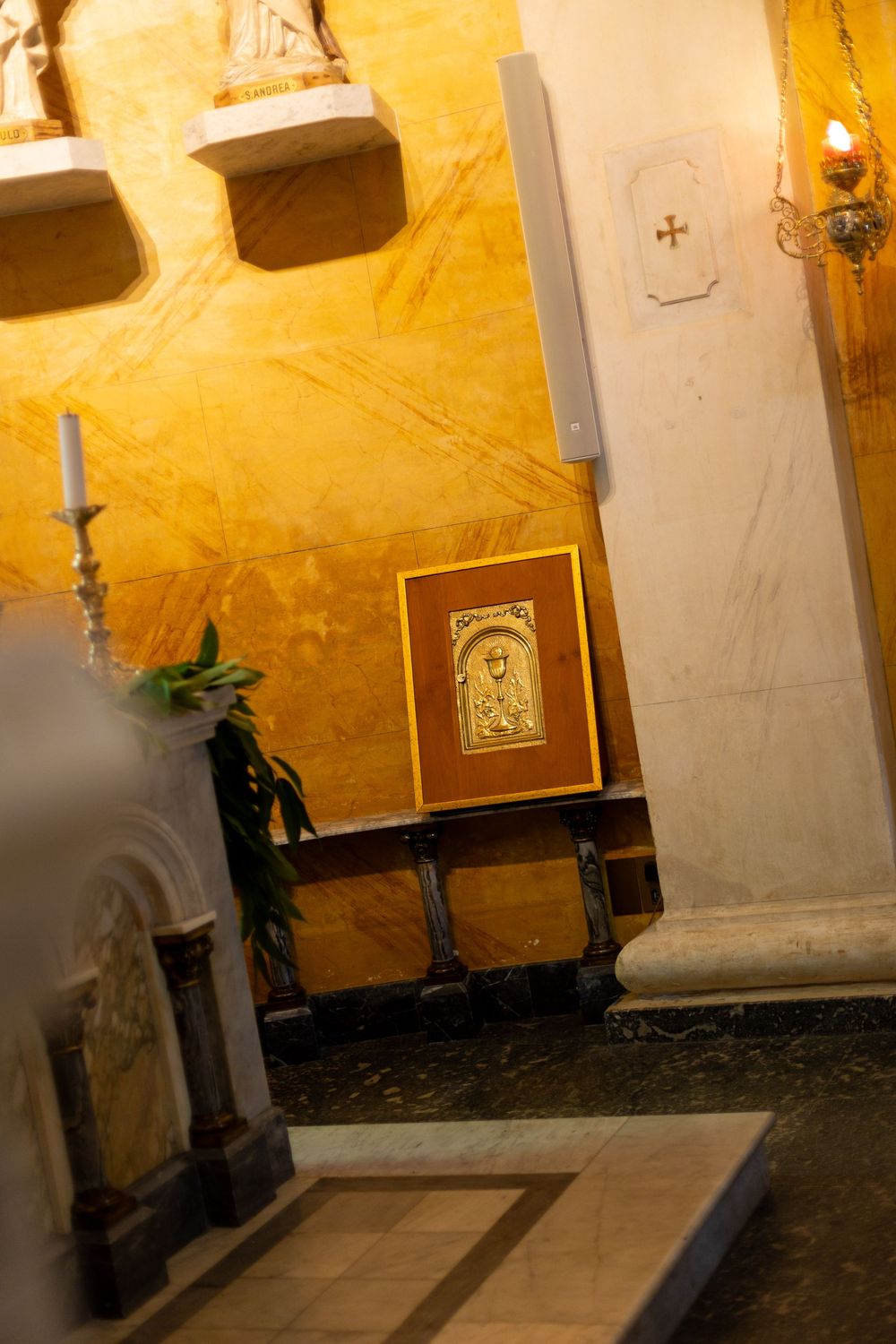 Religious icon displayed on wooden stand against golden yellow wall with candlestick in dimly lit church interior.