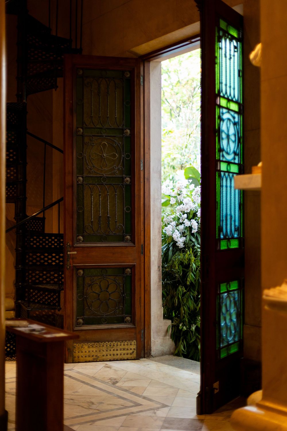 Elegant hallway with ornate wooden doors and green stained glass panels casting warm light in a traditional interior.