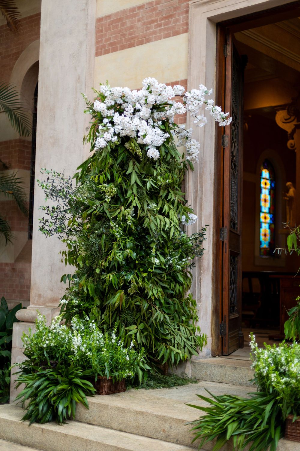 Elegant white floral arrangements with tropical leaves framing an entrance.