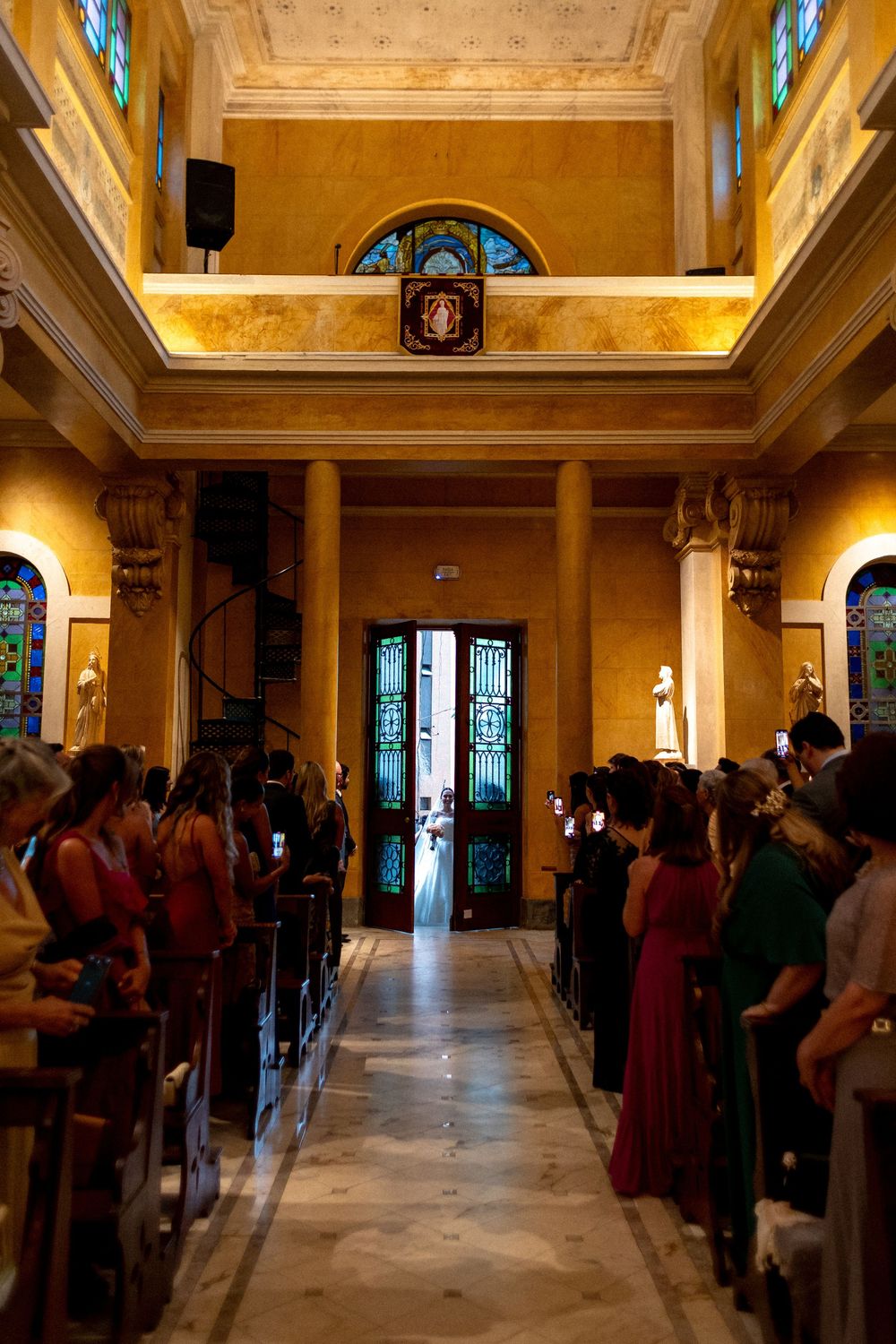 Interior view of a beautiful church with stained glass windows and marble floors filled with wedding guests.