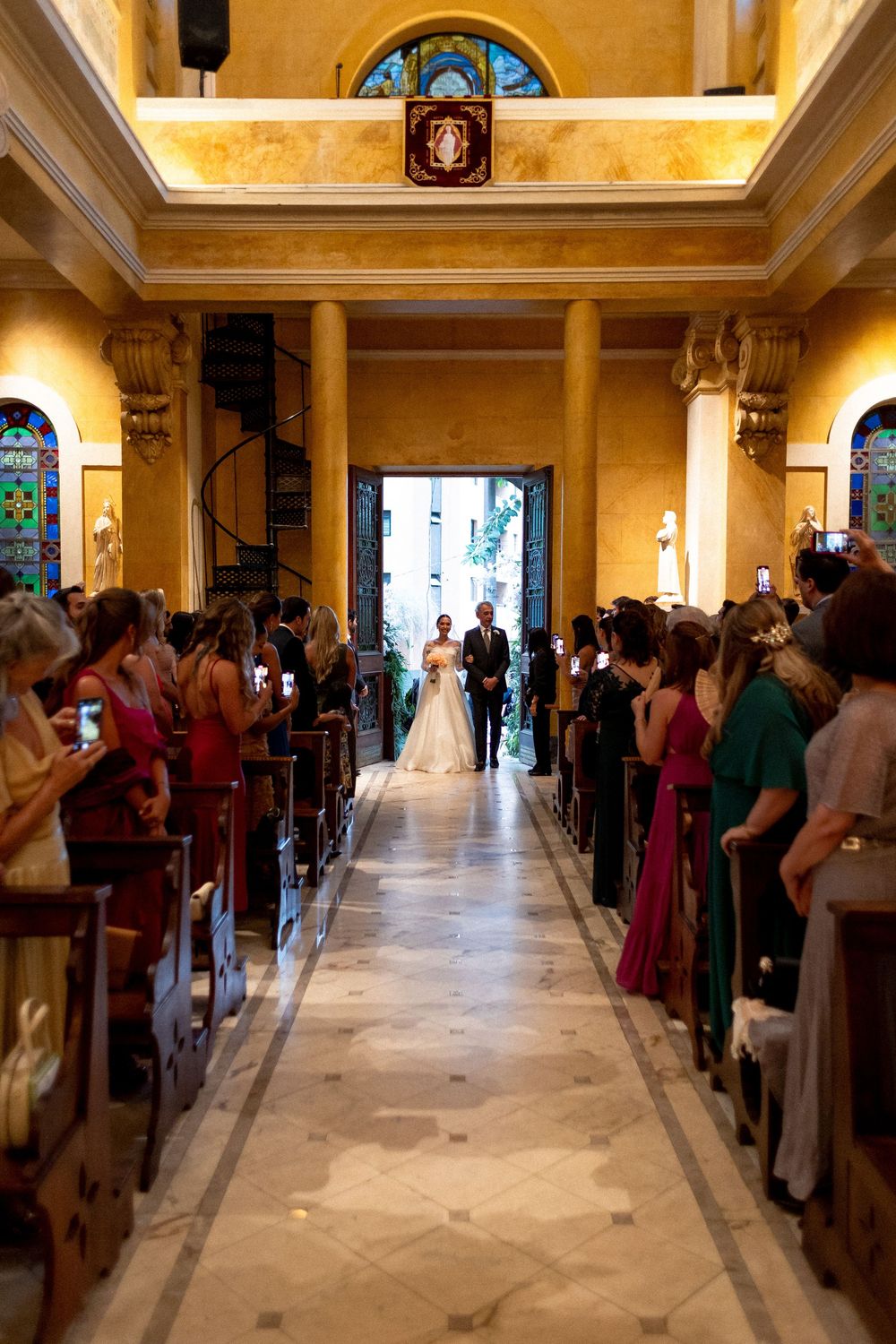 Church interior with marble floors and stained glass windows filled with wedding guests.
