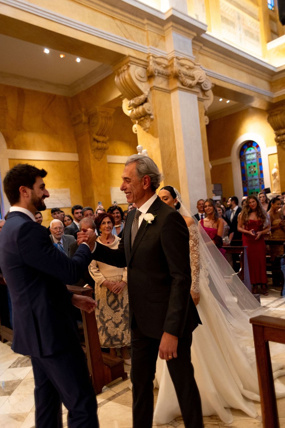 Wedding guests gather in an ornate church hallway with golden walls and classical columns.