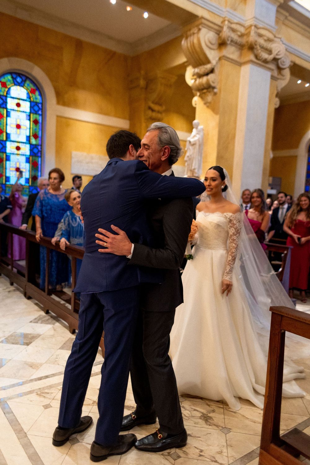 Wedding party members embrace and celebrate on the marble floors of an elegant church interior.