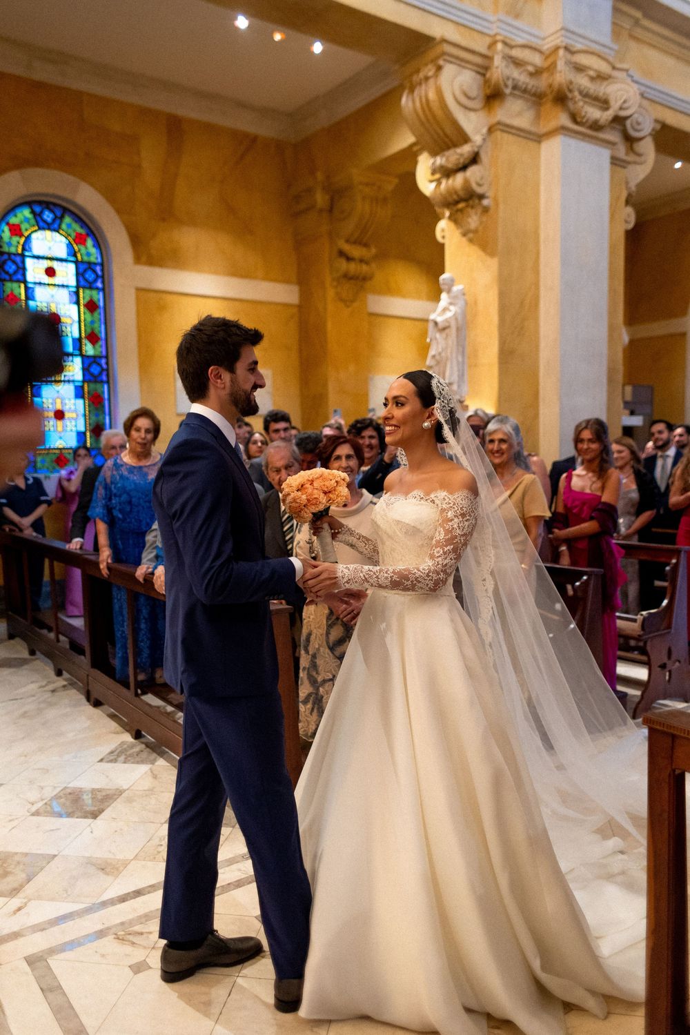 Wedding guests and bridal party gather in a church with stained glass windows during post-ceremony celebrations.