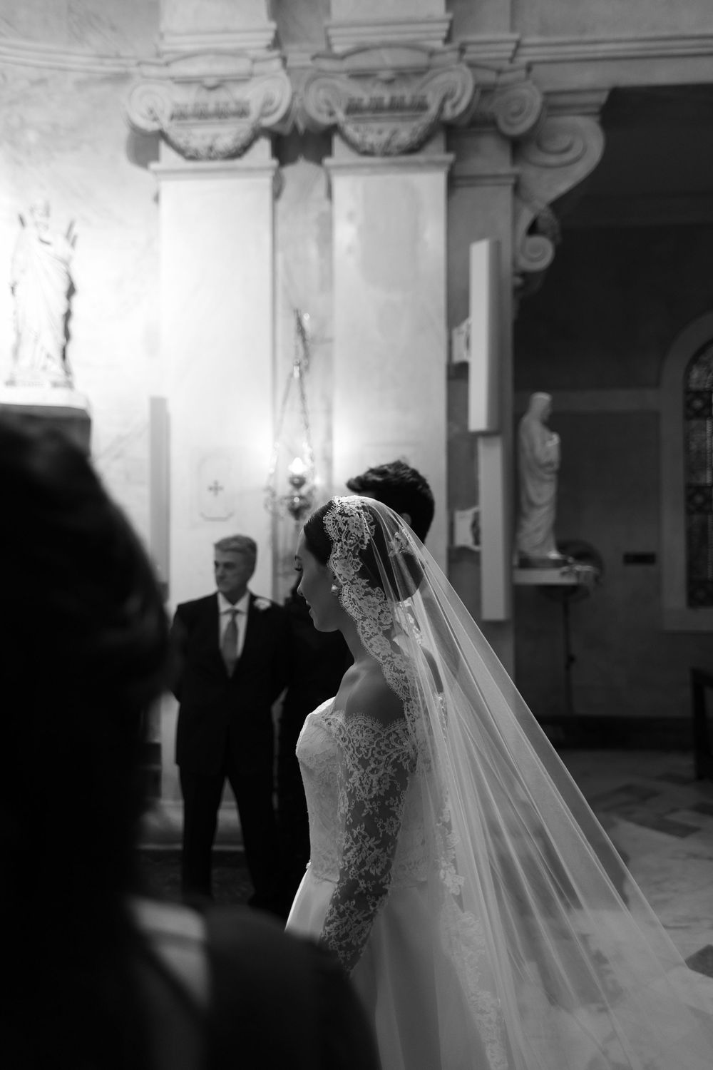 Black and white wedding ceremony photo showing a bride in a lace dress with long flowing veil.