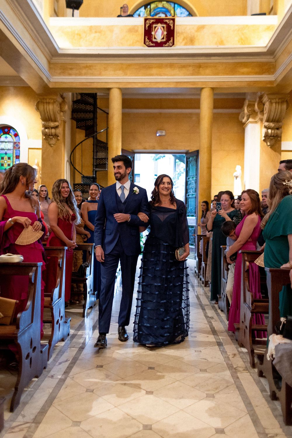 Wedding party members in burgundy dresses and dark suits walking through an elegant church hallway.