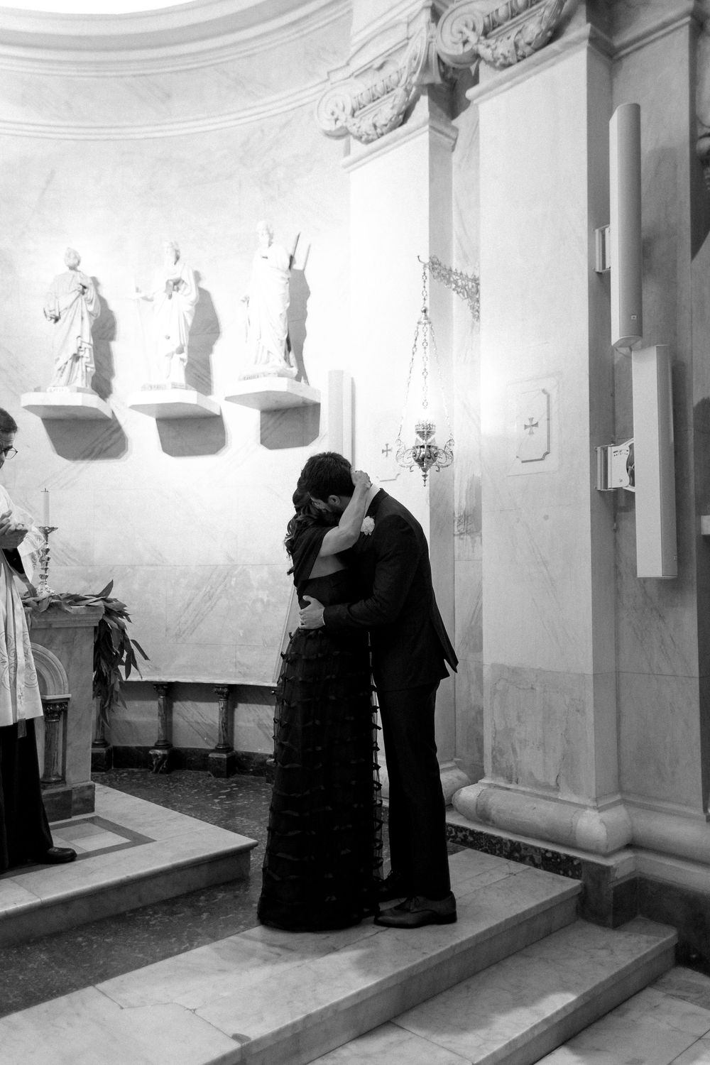 Black and white photo showing figures in dark robes walking through a dimly lit corridor with arched walls.