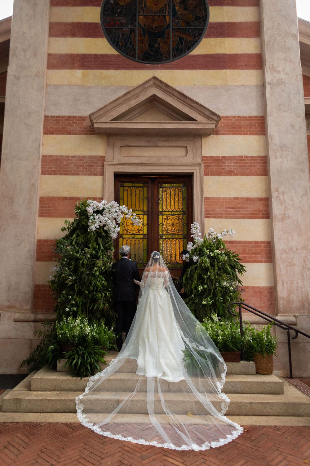 A white wedding veil trails elegantly across church steps with red brick and striped architectural details.