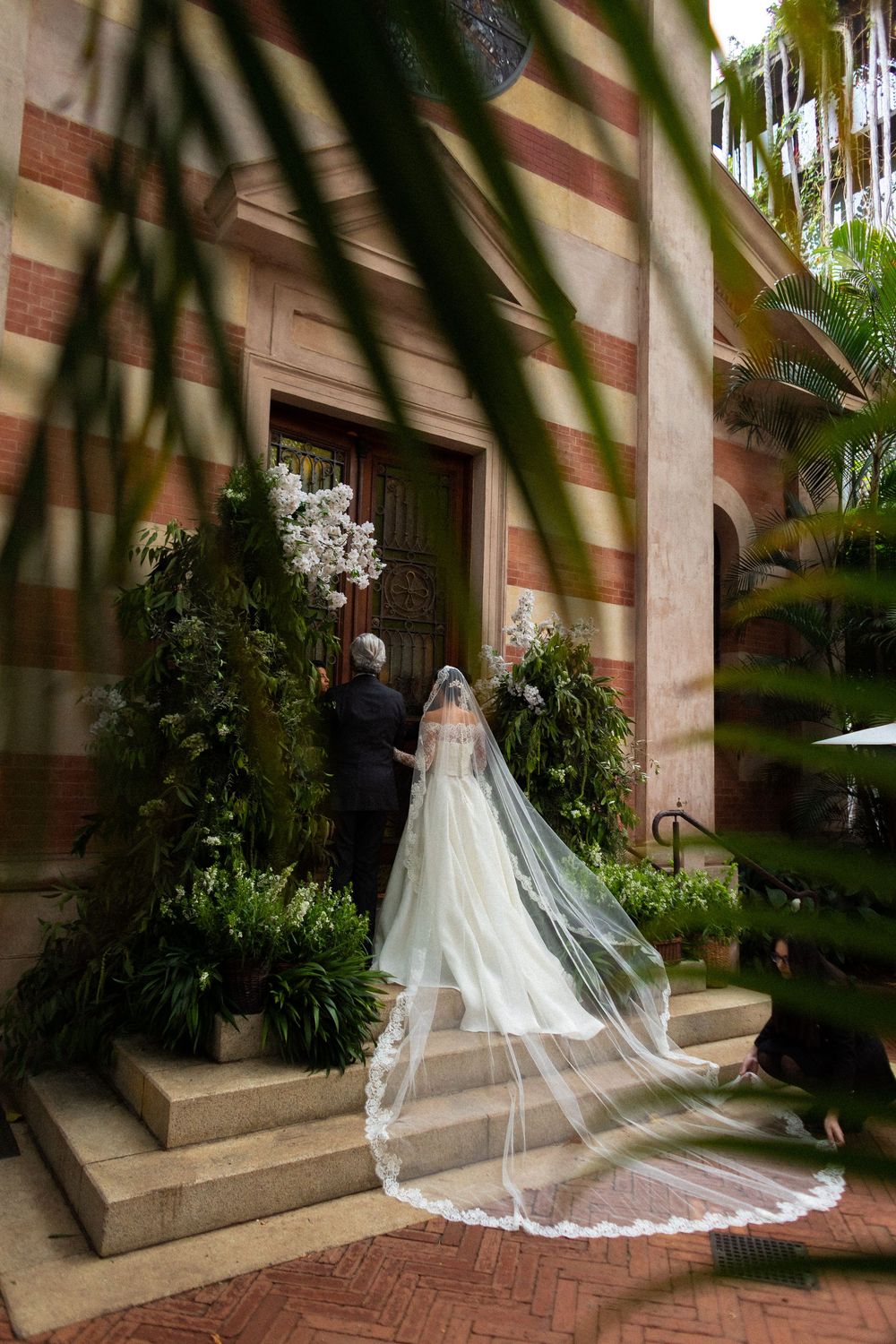 A flowing white wedding dress with cathedral train photographed in sequence against a brick and foliage backdrop.
