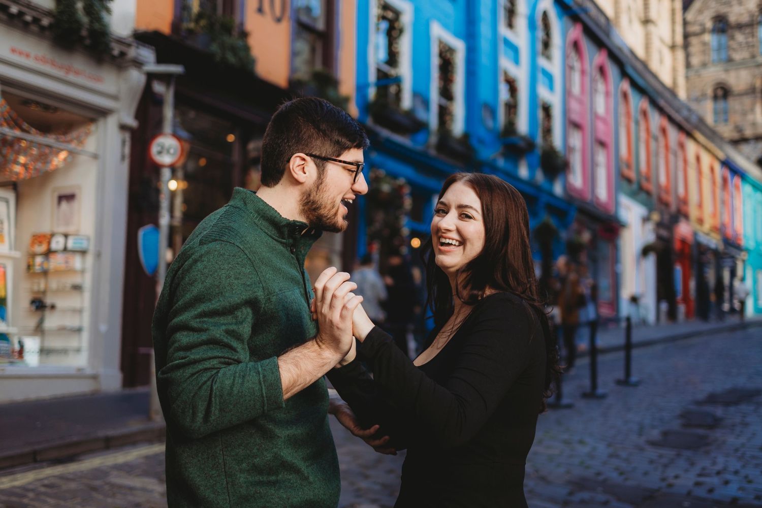 A couple shares a romantic moment on a colorful cobblestone street with vibrant blue and pink buildings in the background.