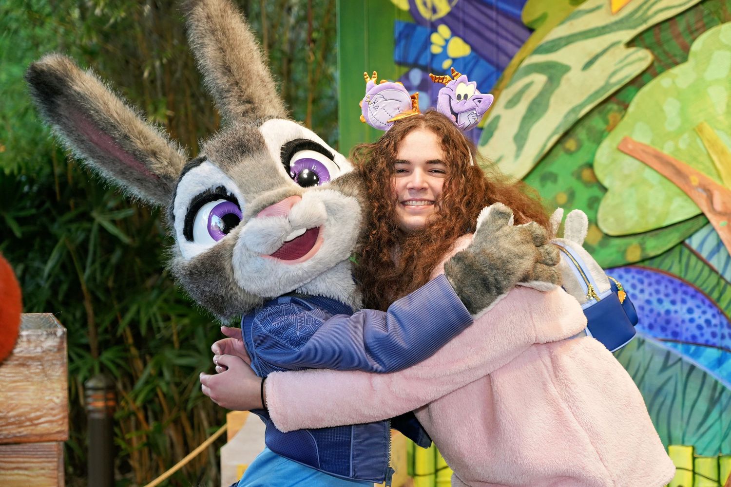 A person in a pink sweater hugs a large costumed character of Judy Hopps from Zootopia at a Disney theme park.