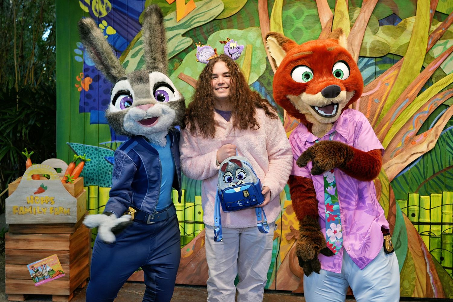 Costumed theme park characters pose together in a vibrant outdoor setting with greenery and colorful decorations. Judy Hops