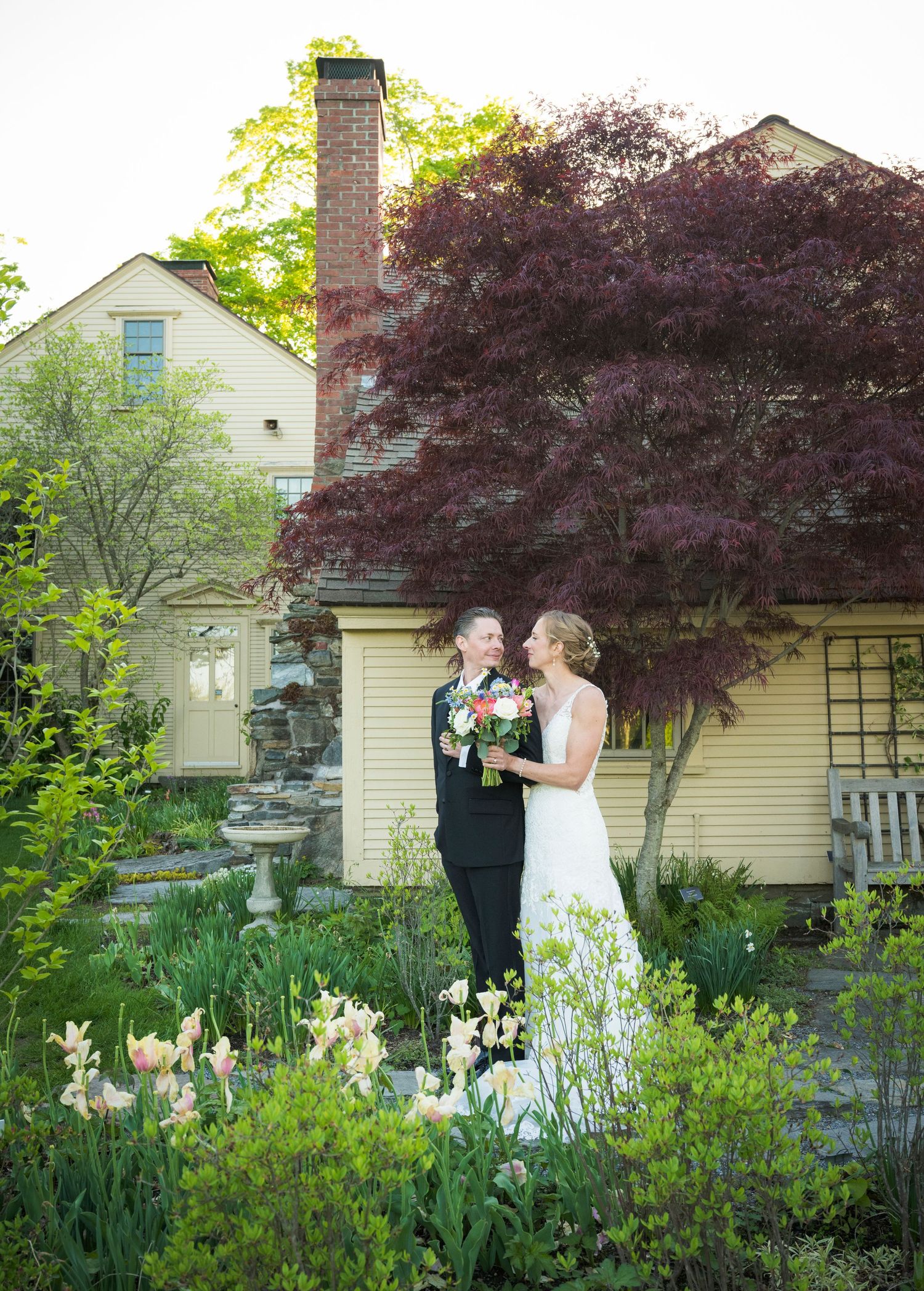 A couple shares romantic moments in a lush garden setting with blooming irises and a charming cottage backdrop.