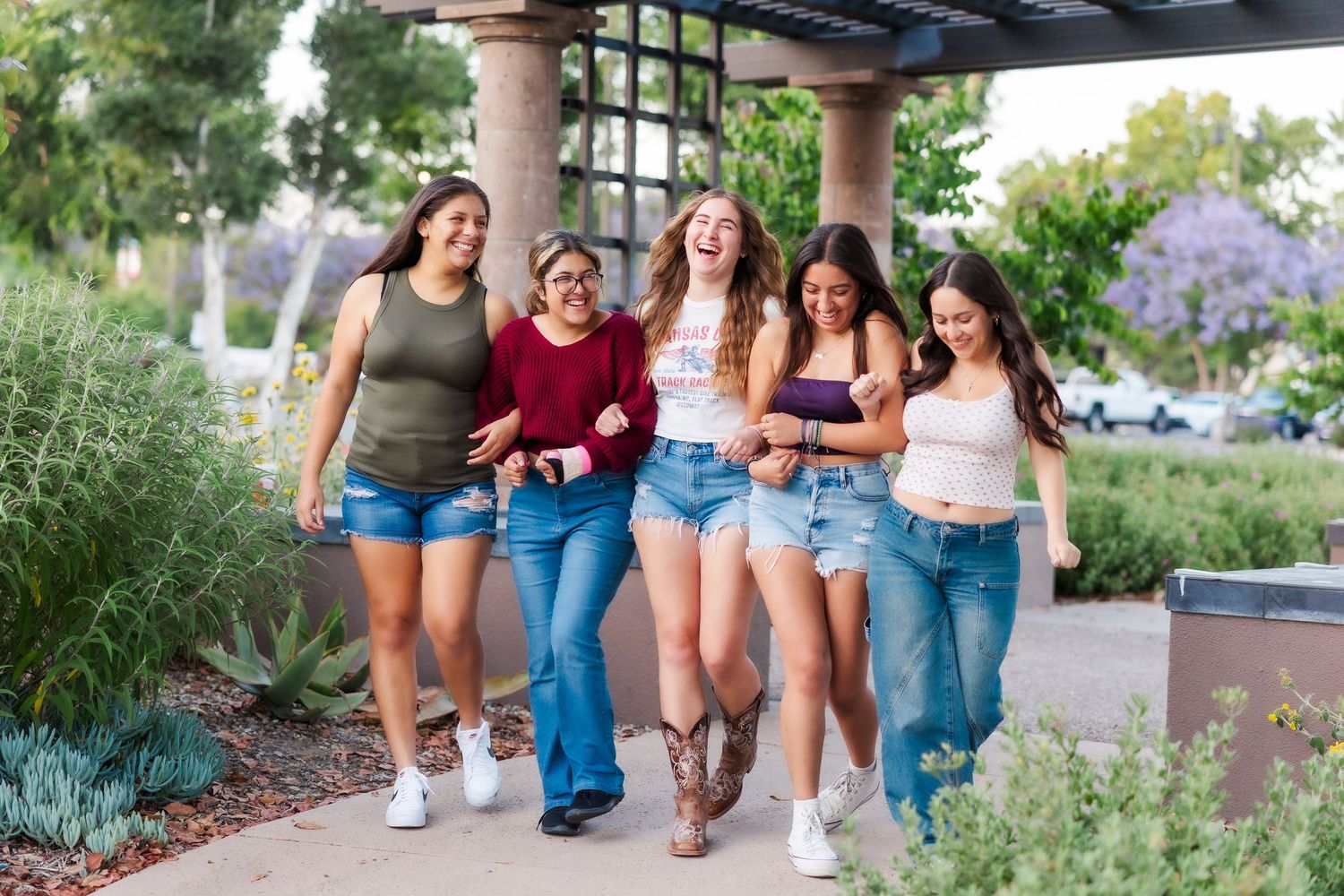 A group of friends walking together and laughing along a garden path on a sunny afternoon.