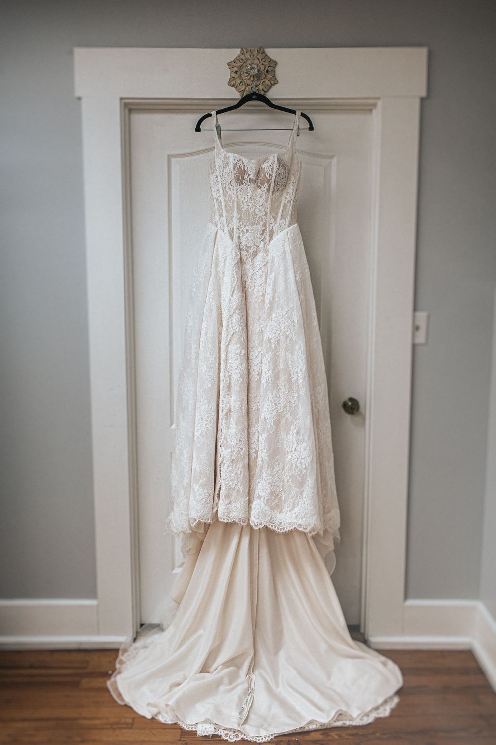 A beautiful two-piece lace wedding gown with flowing train displayed against a white door.