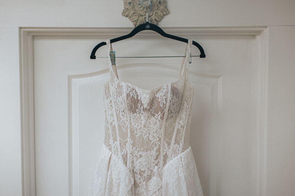 An elegant white lace wedding dress hangs displayed against a white door.