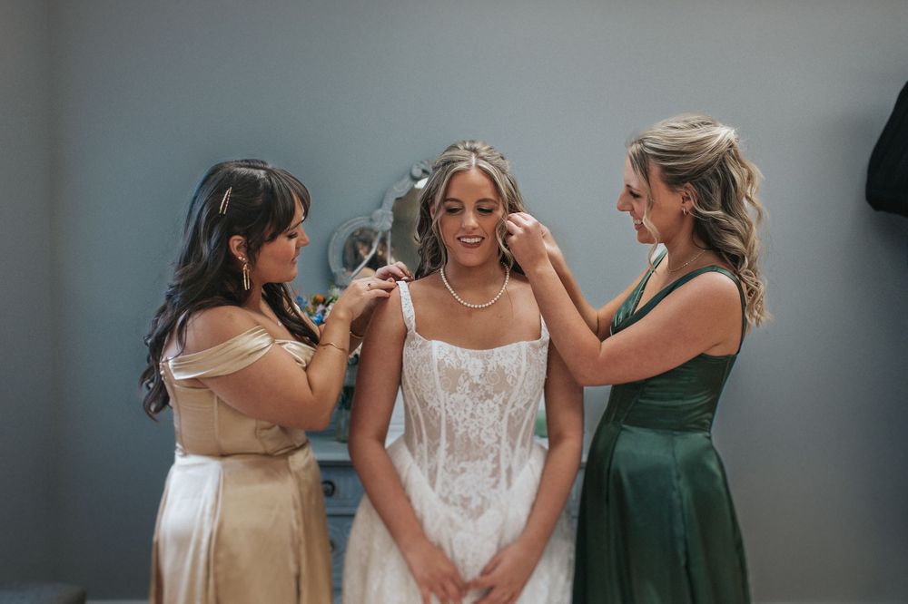 Bridesmaids in elegant dresses help the bride prepare on her wedding day.