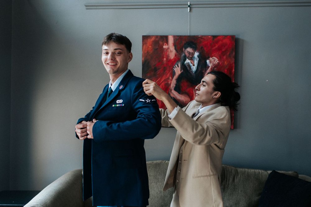 Wedding party members share a playful moment in front of red artwork.