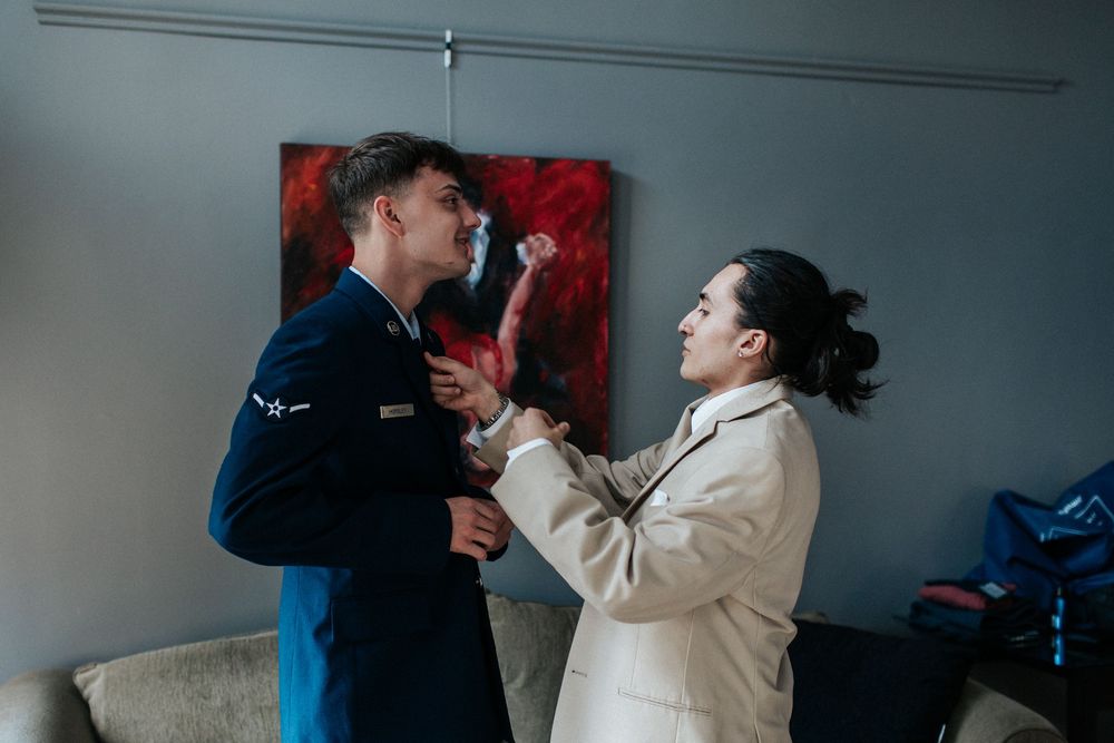 Two people share an animated moment in front of a red wall painting.