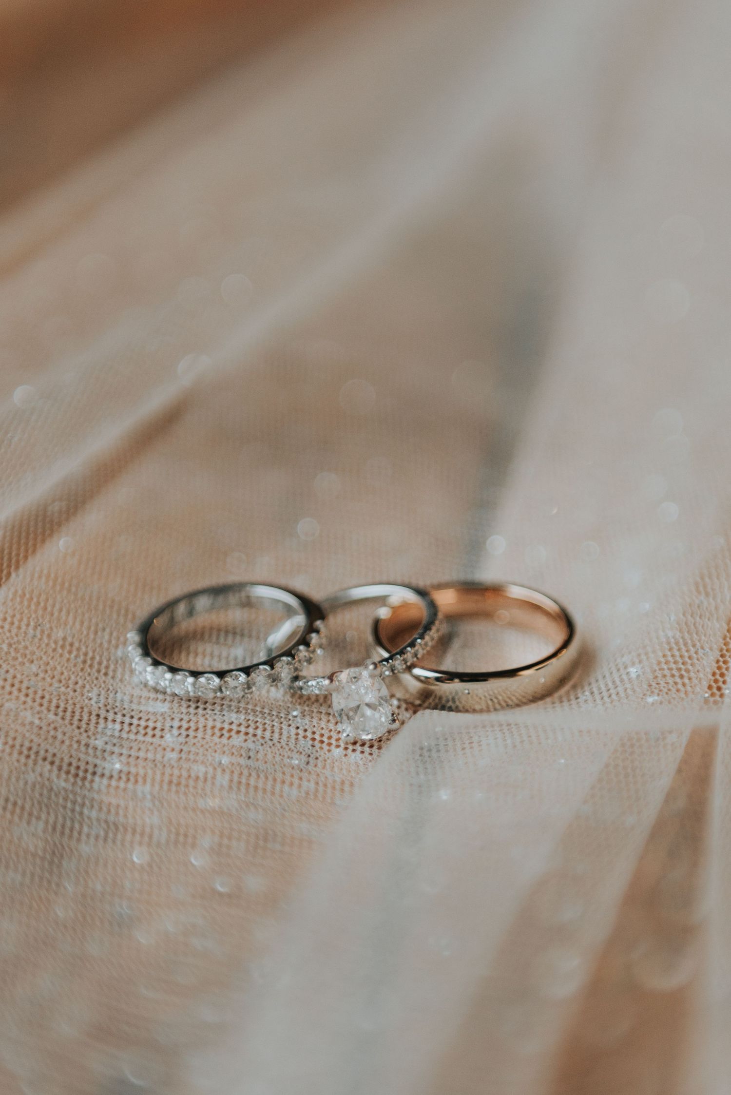 A close-up shot of engagement and wedding rings with diamonds resting on delicate white tulle fabric.