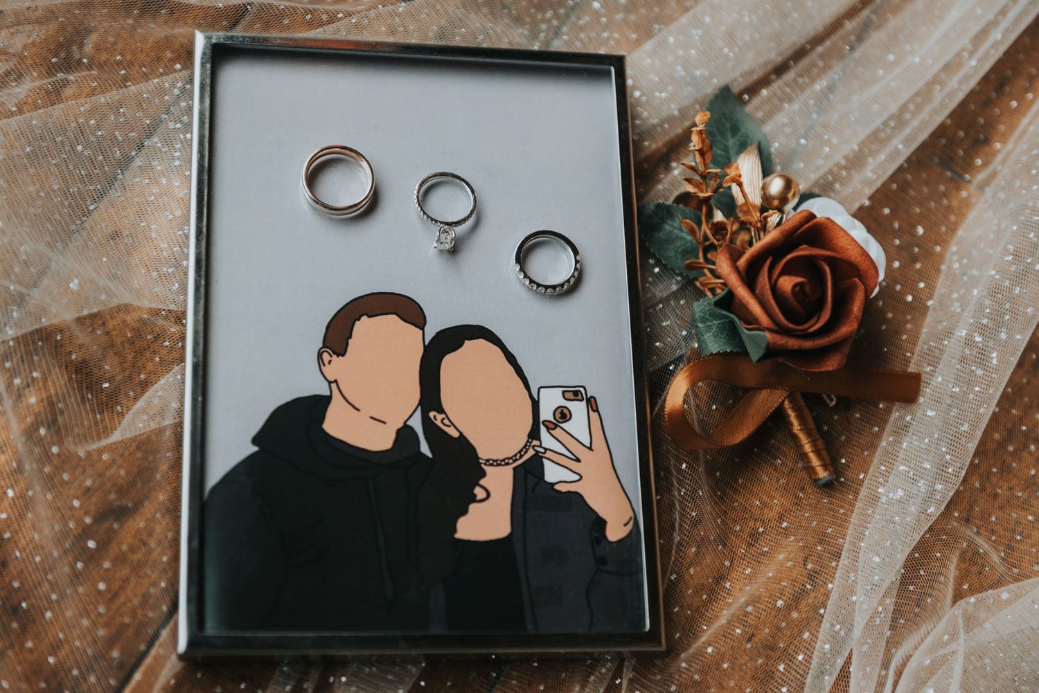 Wedding rings displayed above a minimalist artistic portrait with a copper rose decoration on rustic fabric.