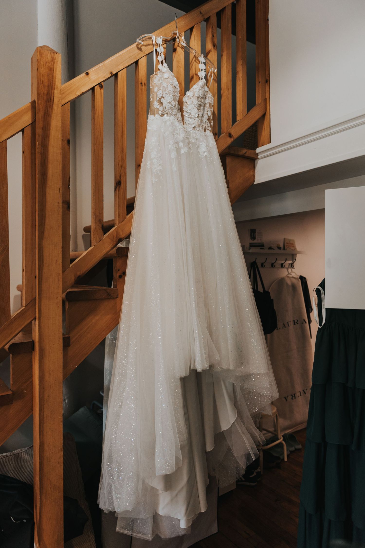 White wedding dress hangs elegantly from wooden staircase railing in natural light.