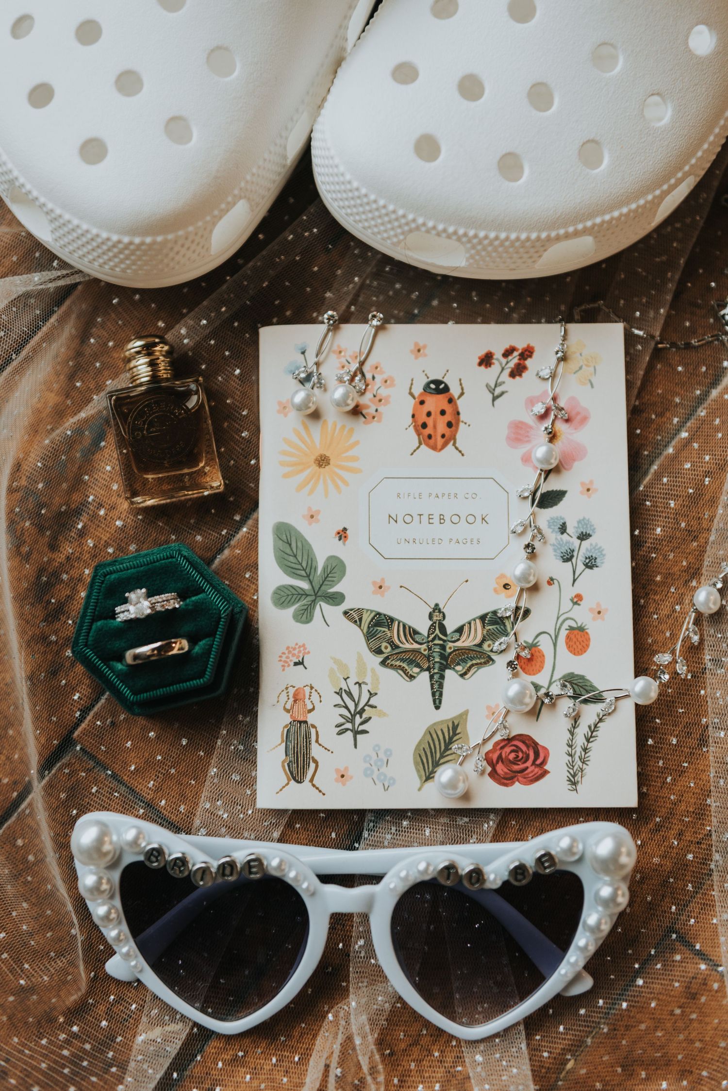 Vintage sunglasses and floral notebooks arranged with wedding rings on a rustic wooden surface.