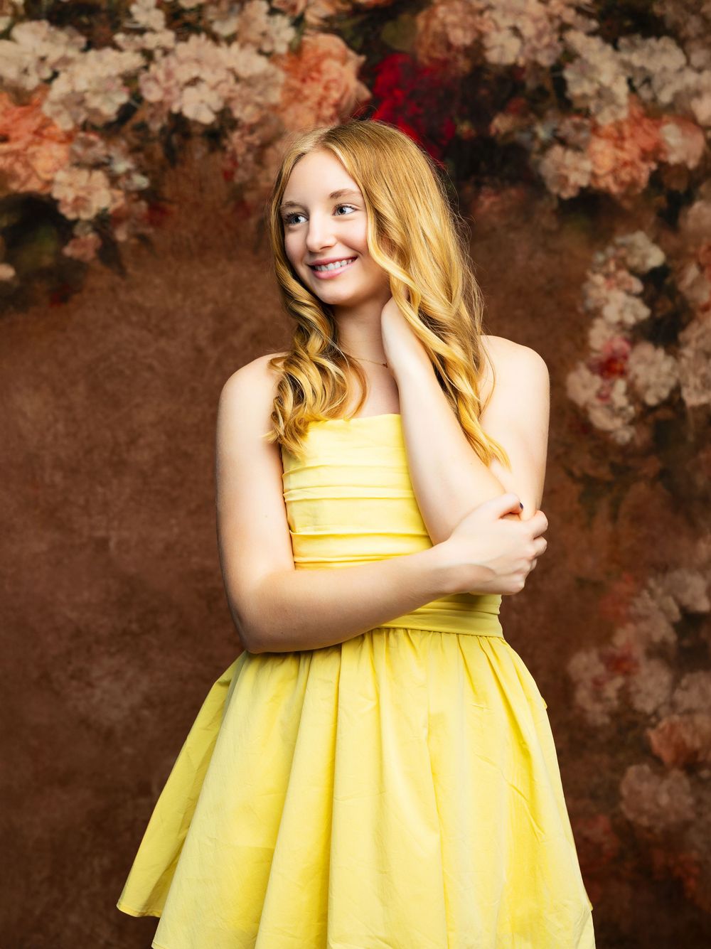A person in a bright yellow sundress poses against a dark floral backdrop in a series of artistic portraits.