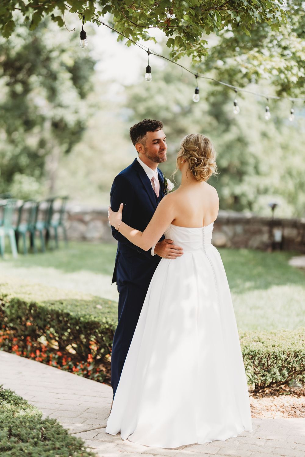 Romantic wedding couple walking along a garden path under hanging lights and trees.