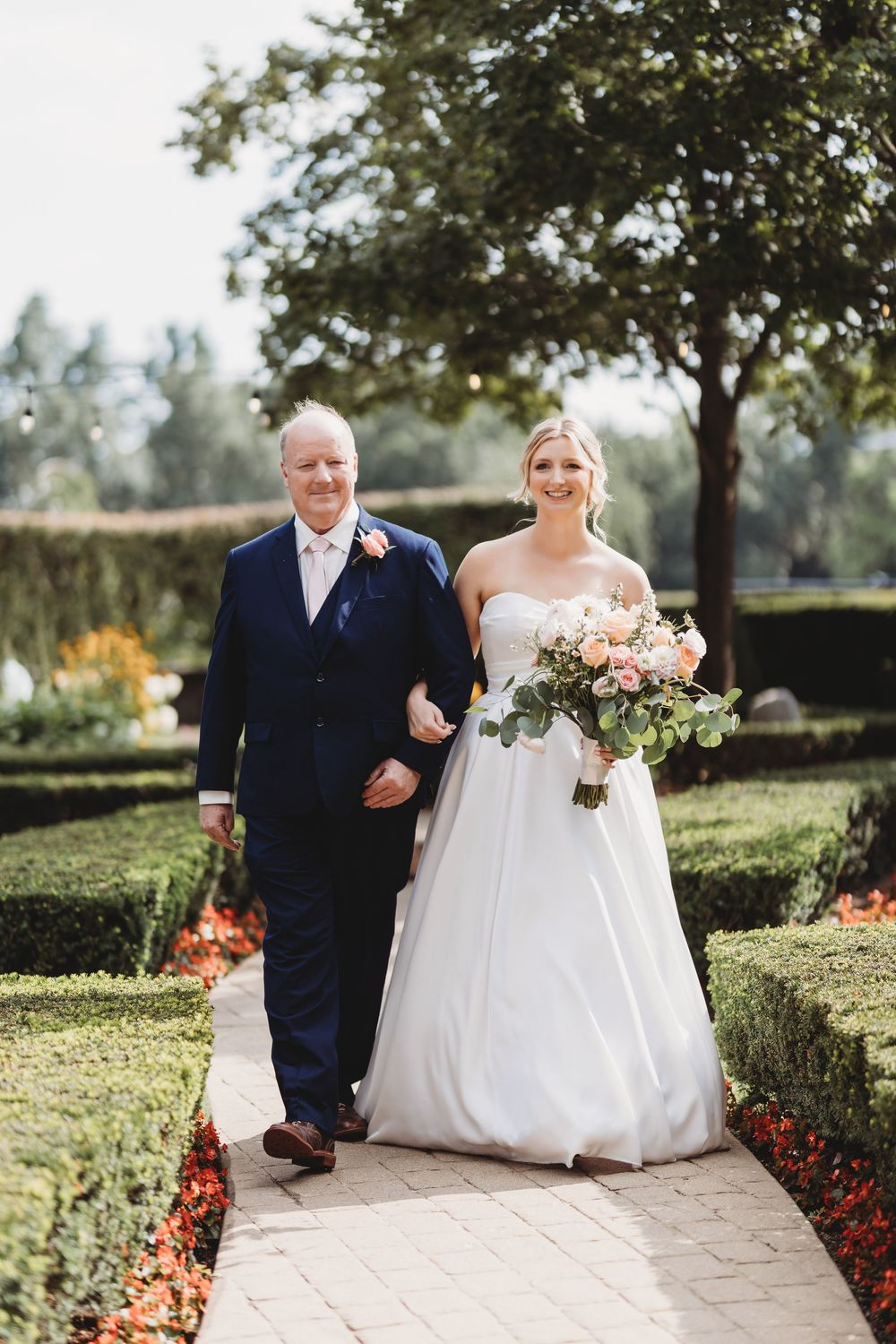 A bride walks down a garden path carrying a blush-colored bouquet on her wedding day.