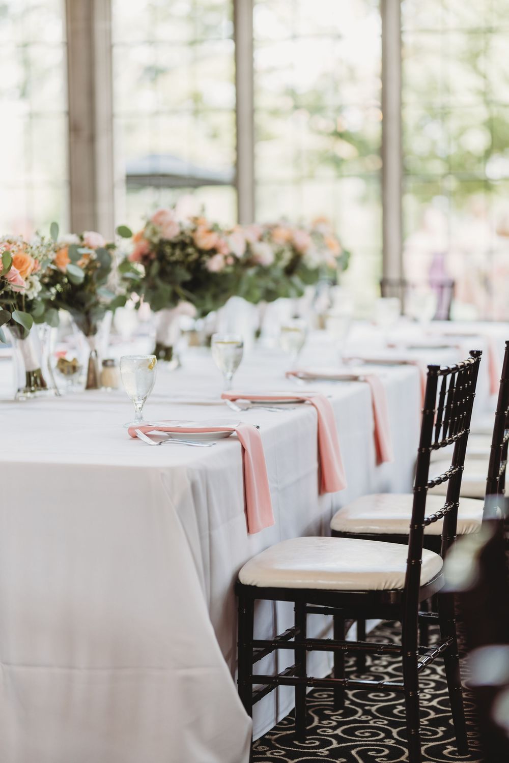 Elegant wedding reception tables set with white linens, pink napkins and floral centerpieces.