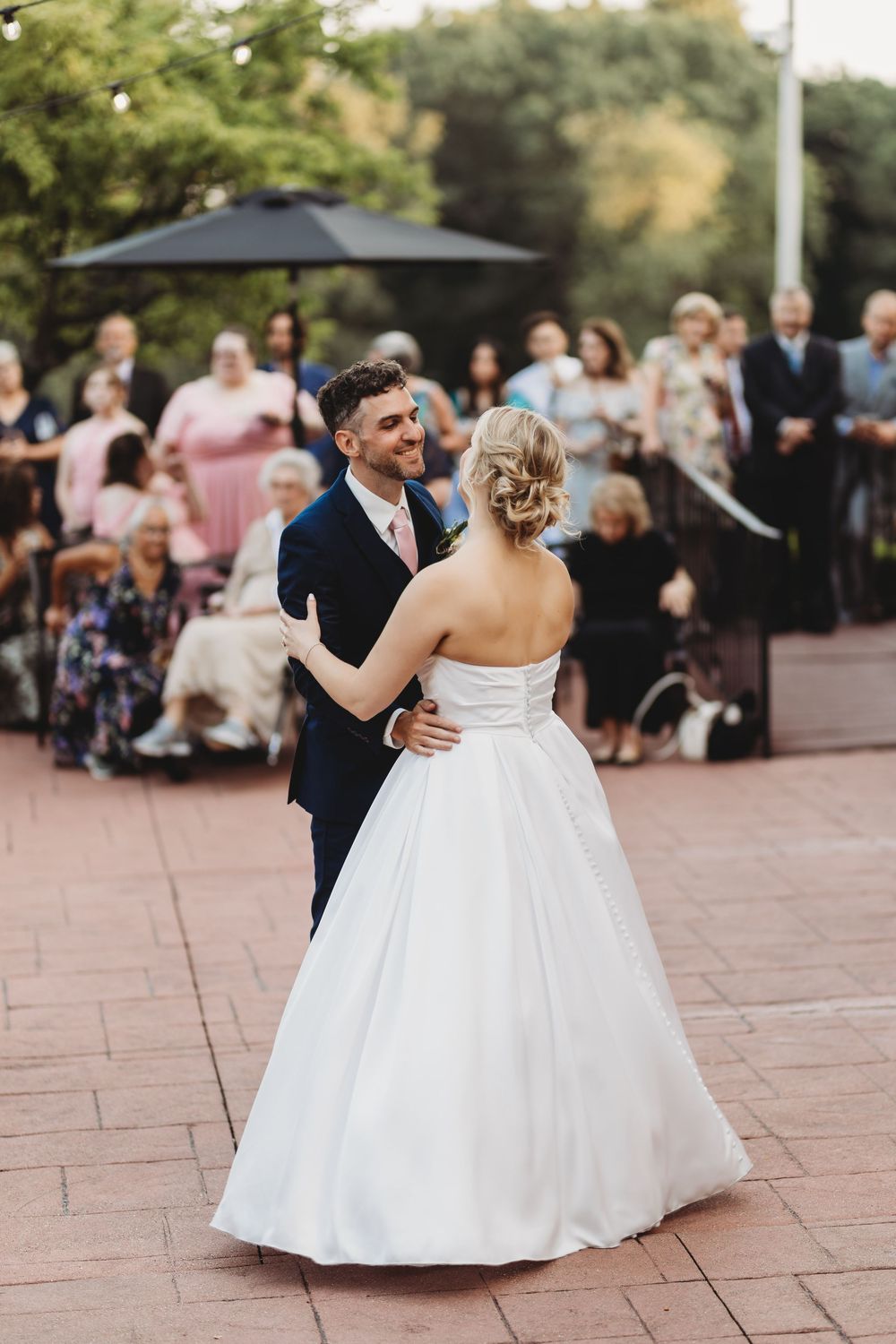 Wedding dance on outdoor patio with guests watching in background at sunset.