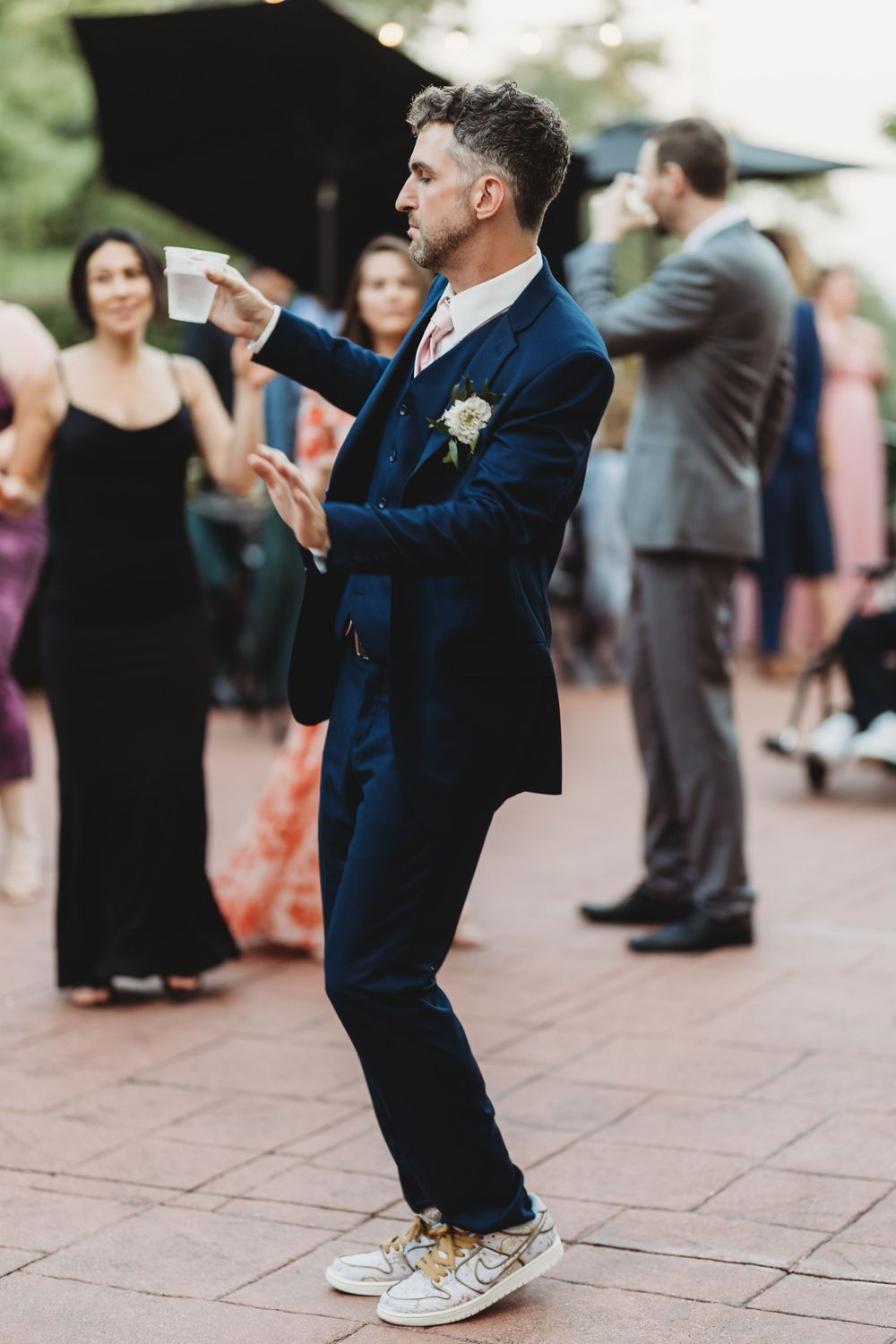 Wedding guests dancing and celebrating on a brick patio during an outdoor reception.