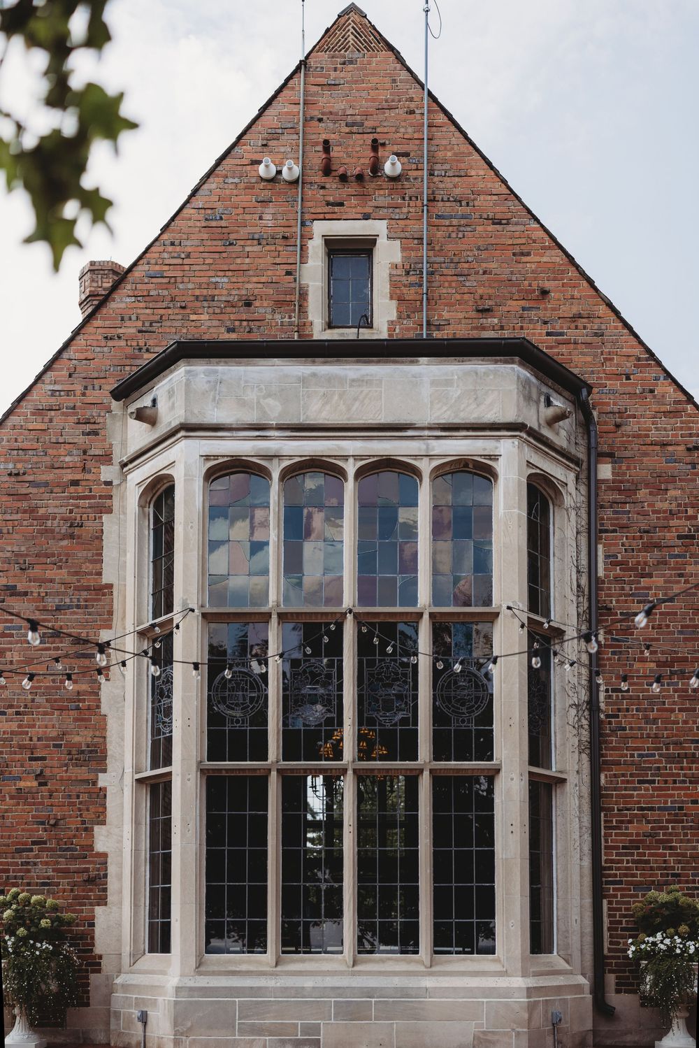 Historic brick building exterior featuring large Tudor-style bay windows with stone trim details.