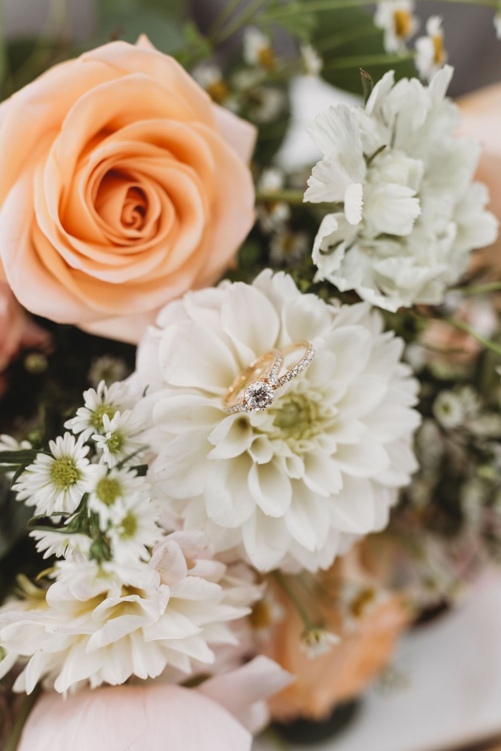Close-up of a peach rose and white dahlia wedding bouquet with a diamond ring.