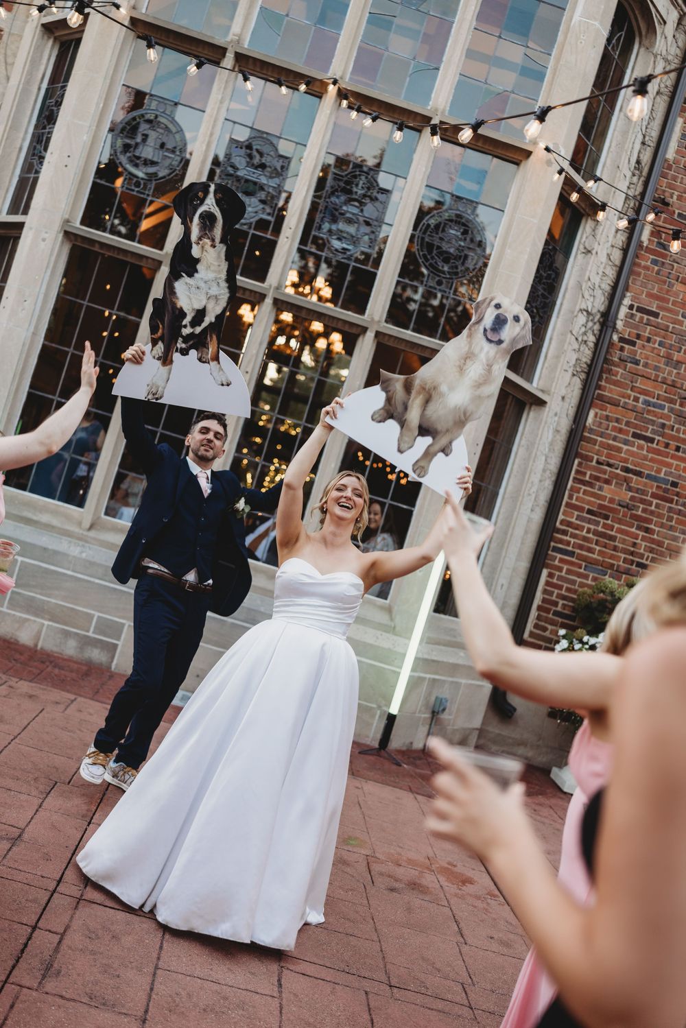 Wedding celebration on a brick patio with large windows and hanging lights at dusk.
