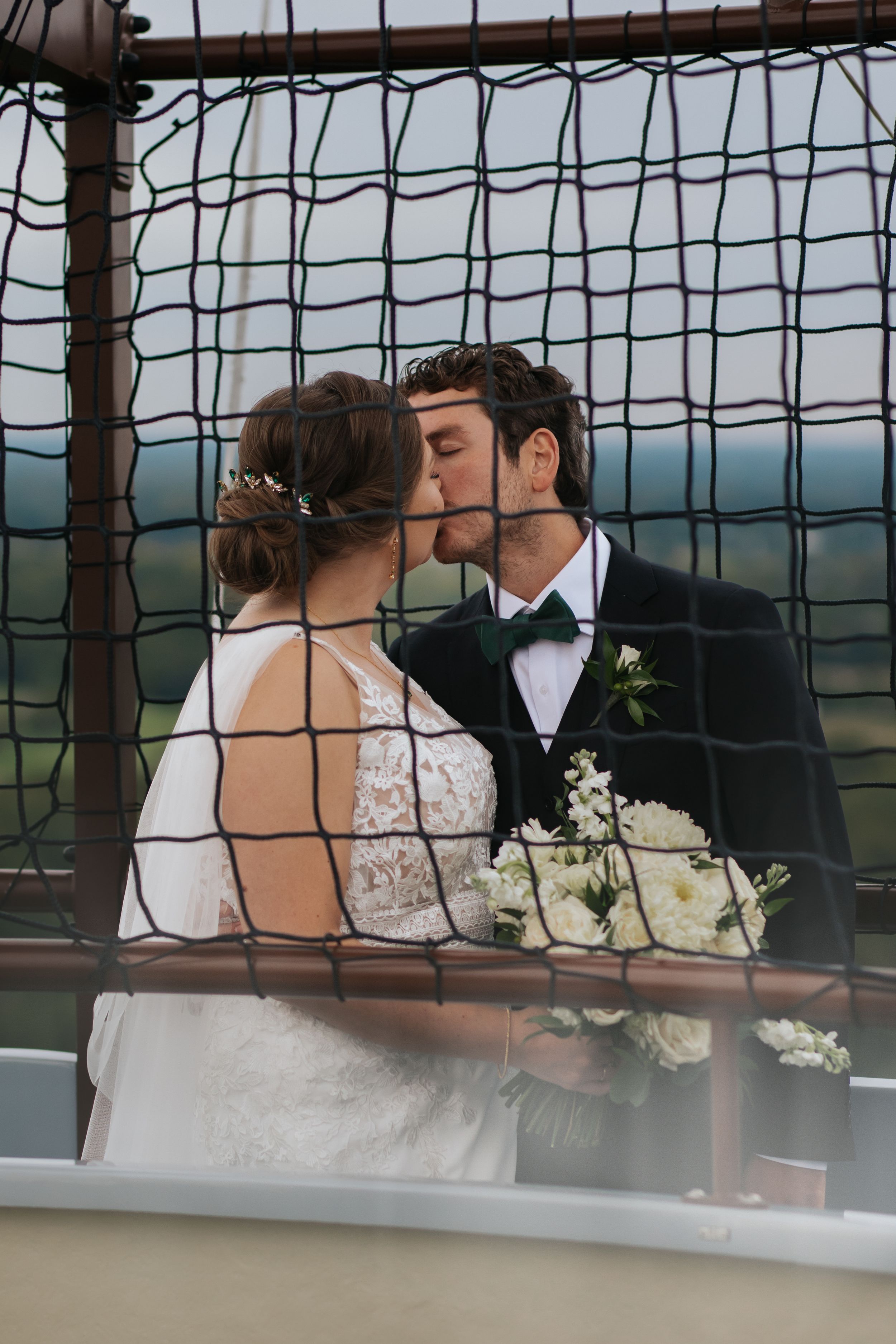 A tender wedding moment captured through geometric mesh patterns with scenic backdrop.