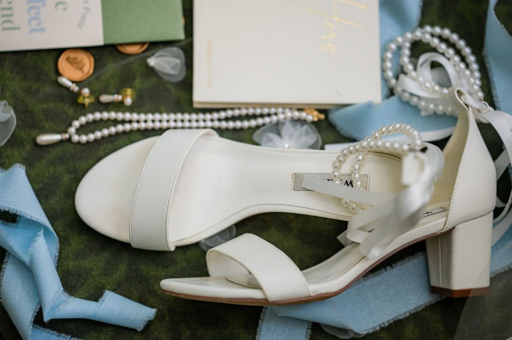 White bridal sandals and accessories arranged artistically on a blue surface.