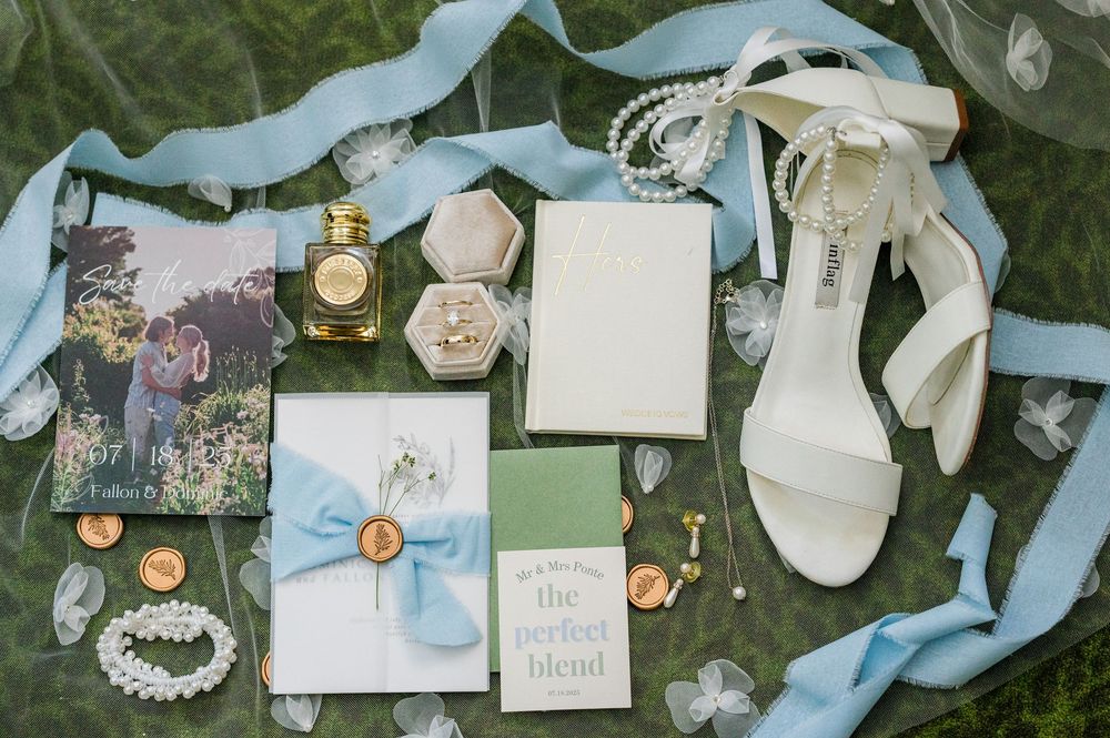 Wedding details including blue ribbons, jewelry, and delicate accessories laid out on grass.