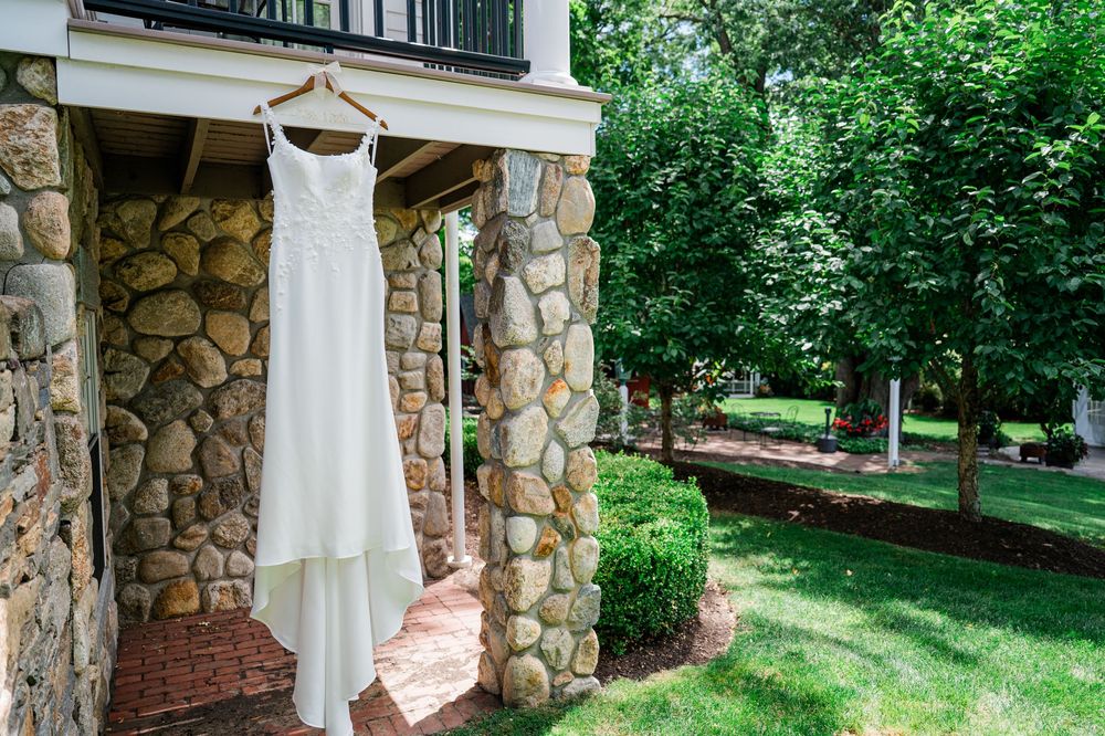 Elegant white wedding dress displayed against stone pillars and greenery outdoors.